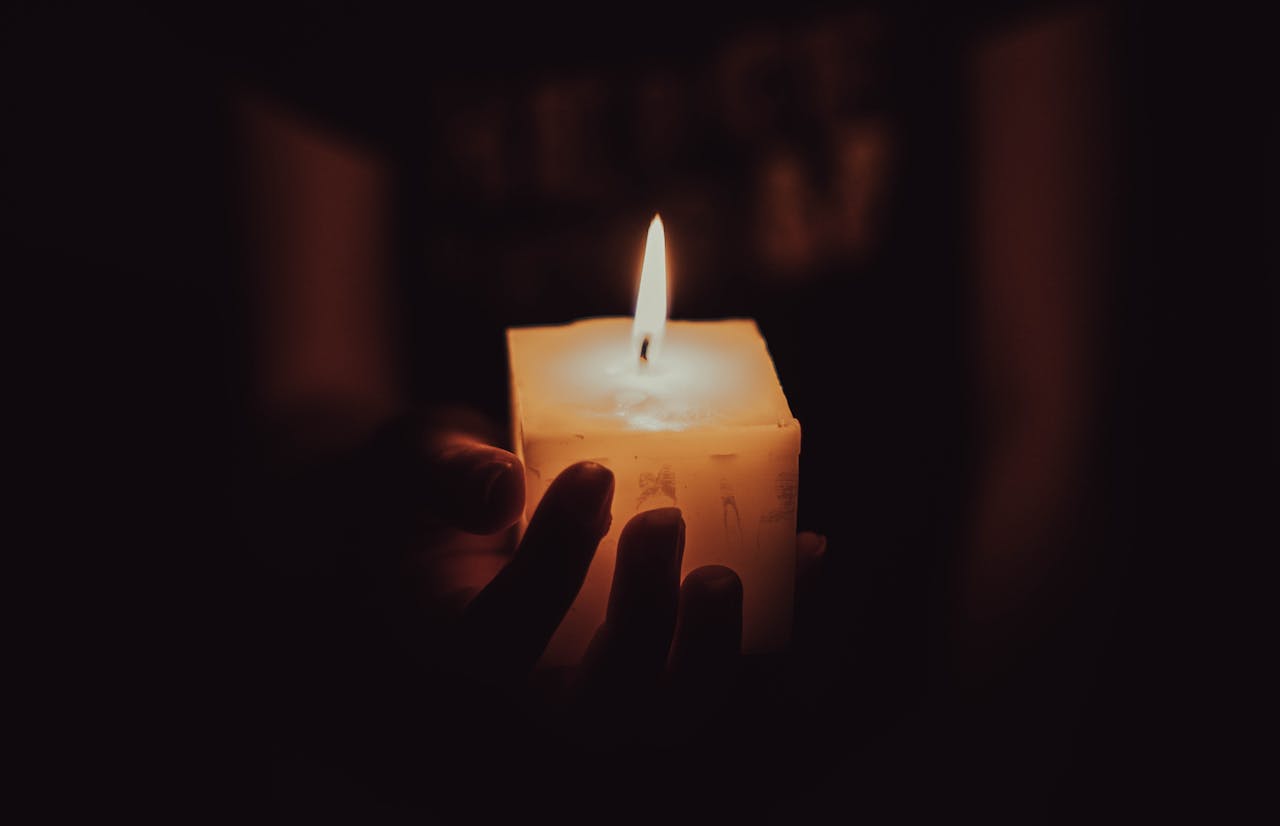 services-02 A close-up image of hands holding a lighted candle in a dimly lit setting, creating a warm and serene ambiance.